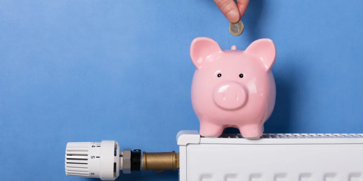 a person's hand inserting coin in piggy bank on radiator