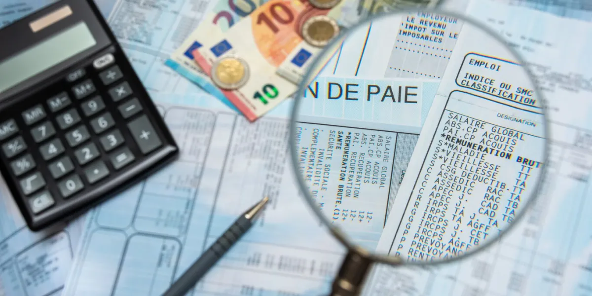 blurred french payroll with a calculator, a pen, euro cash, and a magnifying glass sharp focus only through the magnifying glass