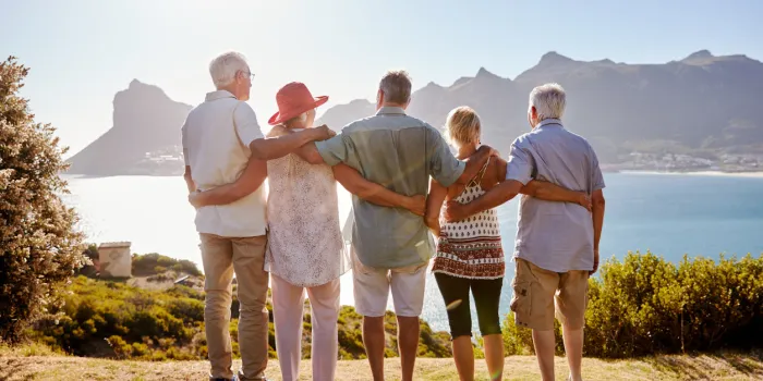 rear view of senior friends visiting tourist landmark on group vacation standing on wall