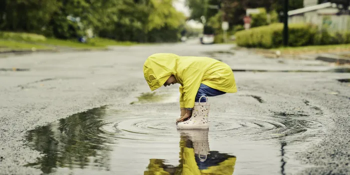 a funny cute baby girl wearing yellow waterproof coat and boots playing in the rain