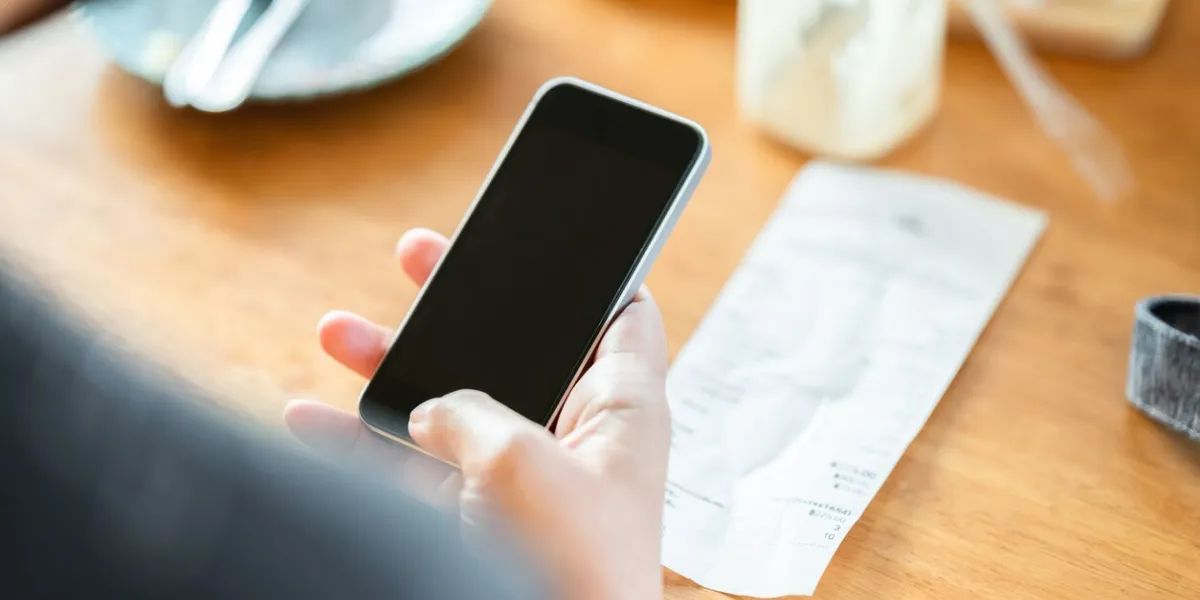 closeup woman hand use the smart phone after meal in the coffee shop, with bill of food and drink on the table, scan or online payment, bill calculating concept