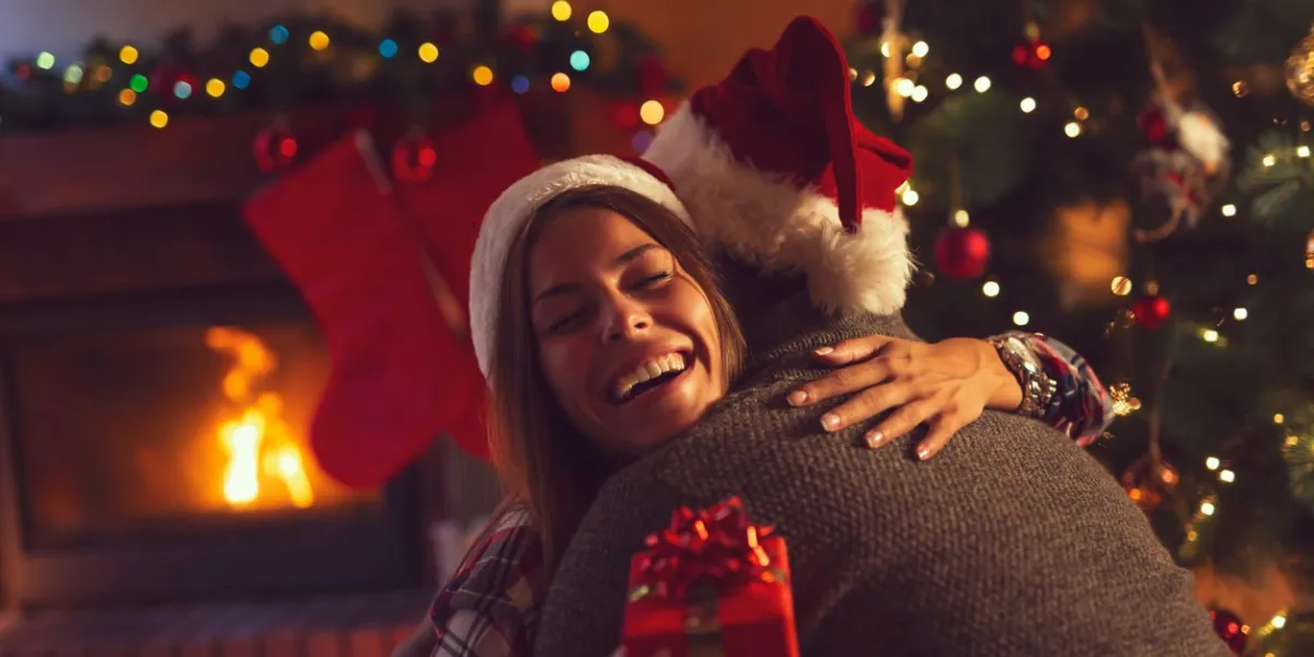 young couple in love sitting by the fireplace and nicely decorated christmas tree, exchanging christmas presents