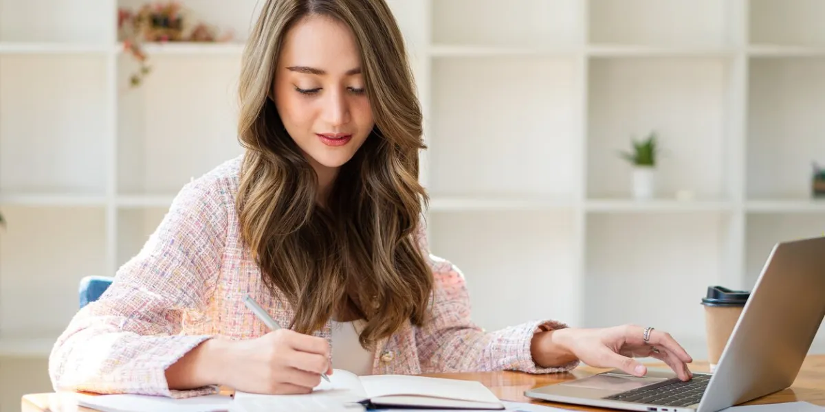 smiling beautiful asian businesswoman analyzing charts and graphs showing market changes using laptop at company desk reading financial charts
