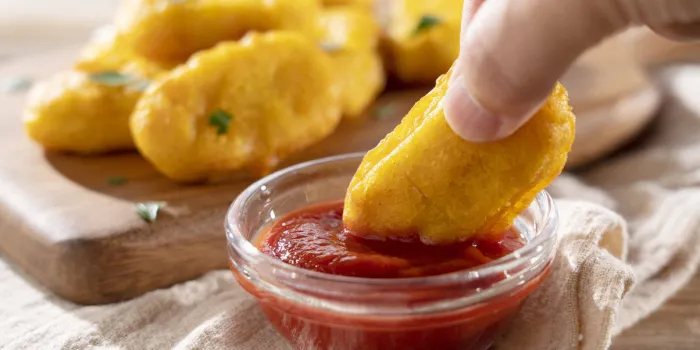 dipping chicken nuggets held in a man's hand into ketchup in a glass bowl