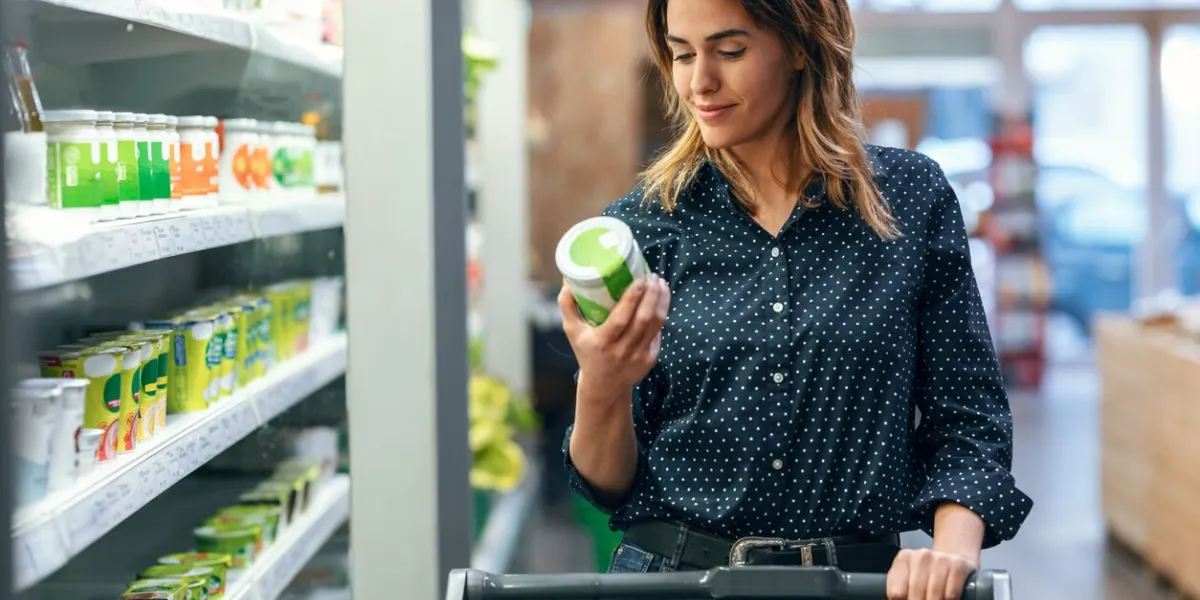 shot of beauty woman walking with shopping cart while taking products from shelf at the grocery