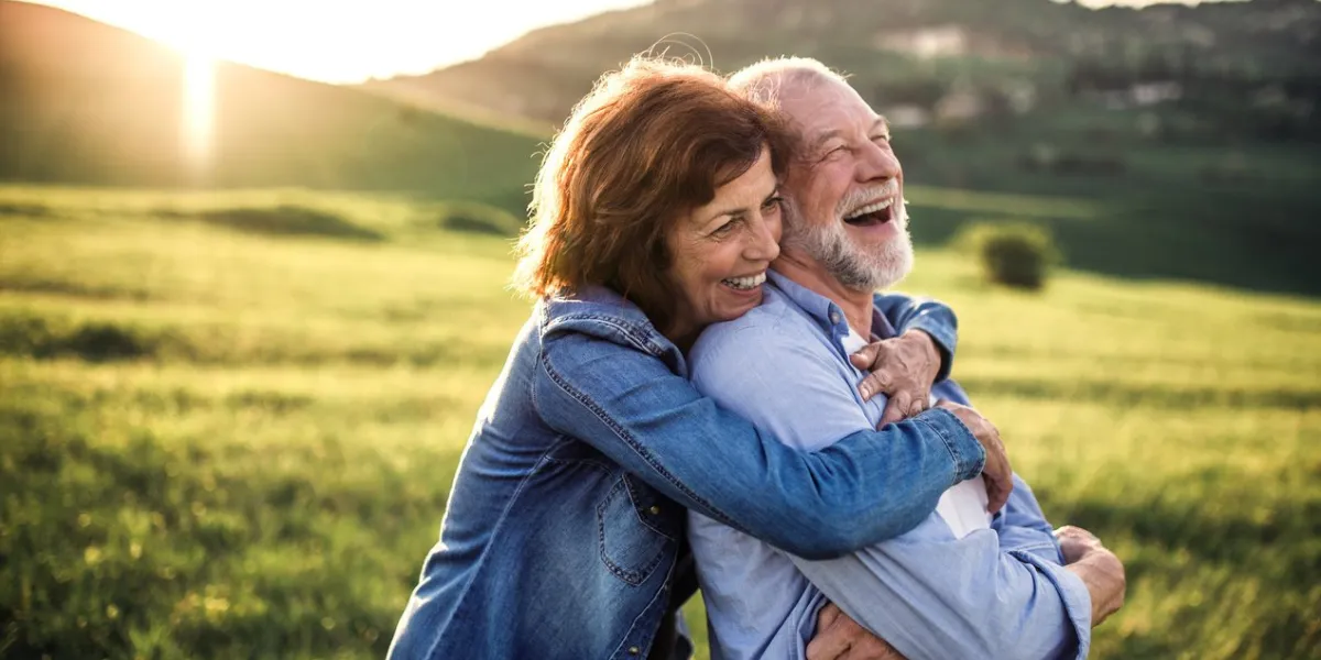 happy senior couple outside in spring nature, hugging at sunset side view