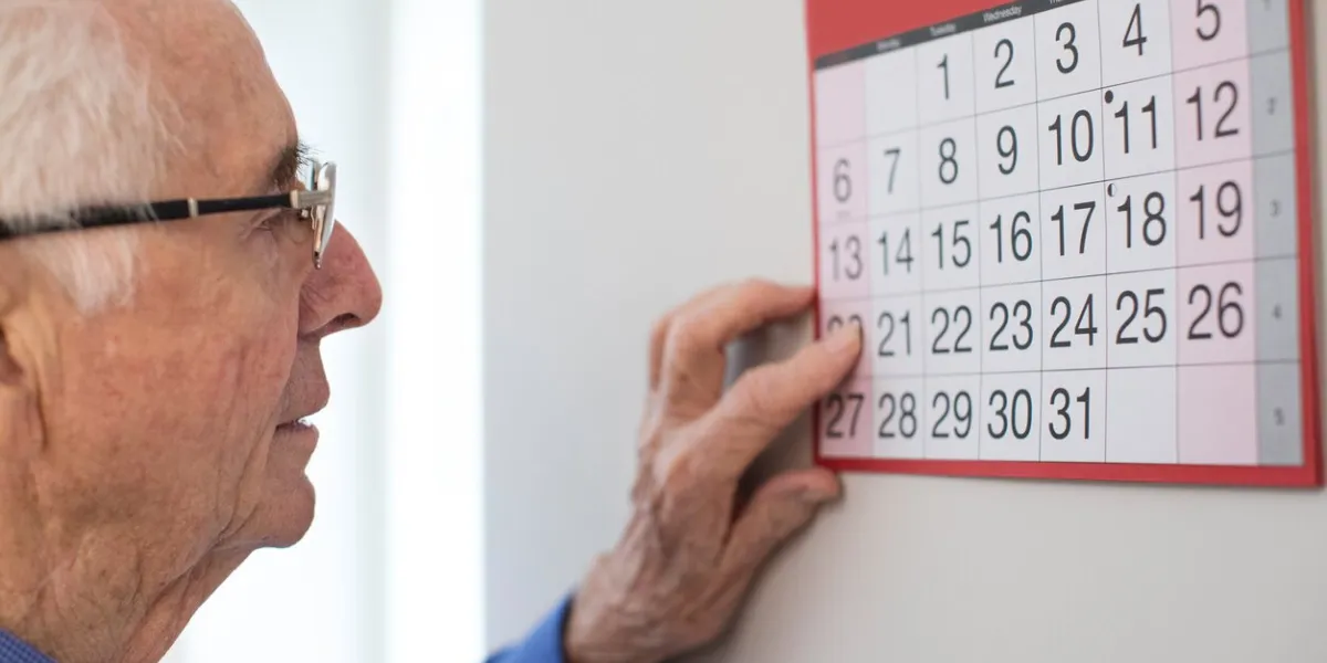 confused senior man with dementia looking at wall calendar