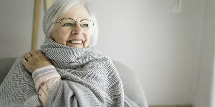 a portrait of elderly woman sit on the sofa at home with warm clothe