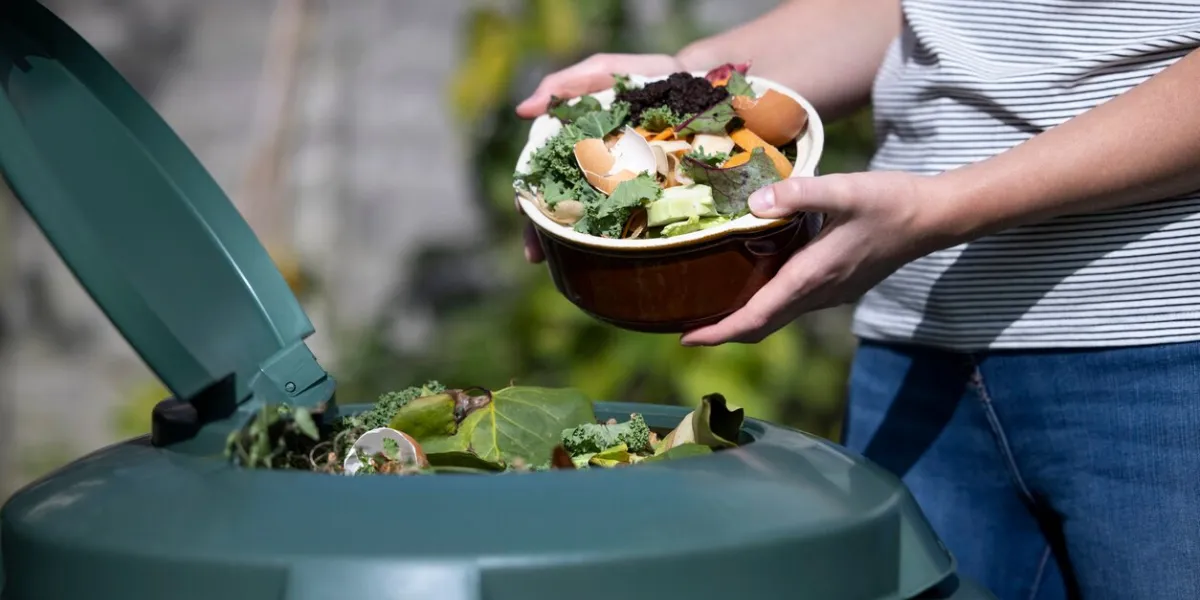 close up of woman emptying food waste into garden composter at home
