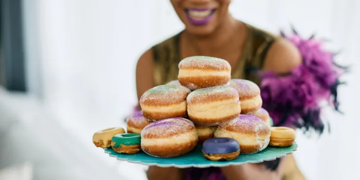 close-up of african american woman with plate of donuts sprinkled with traditional mardi gras colors