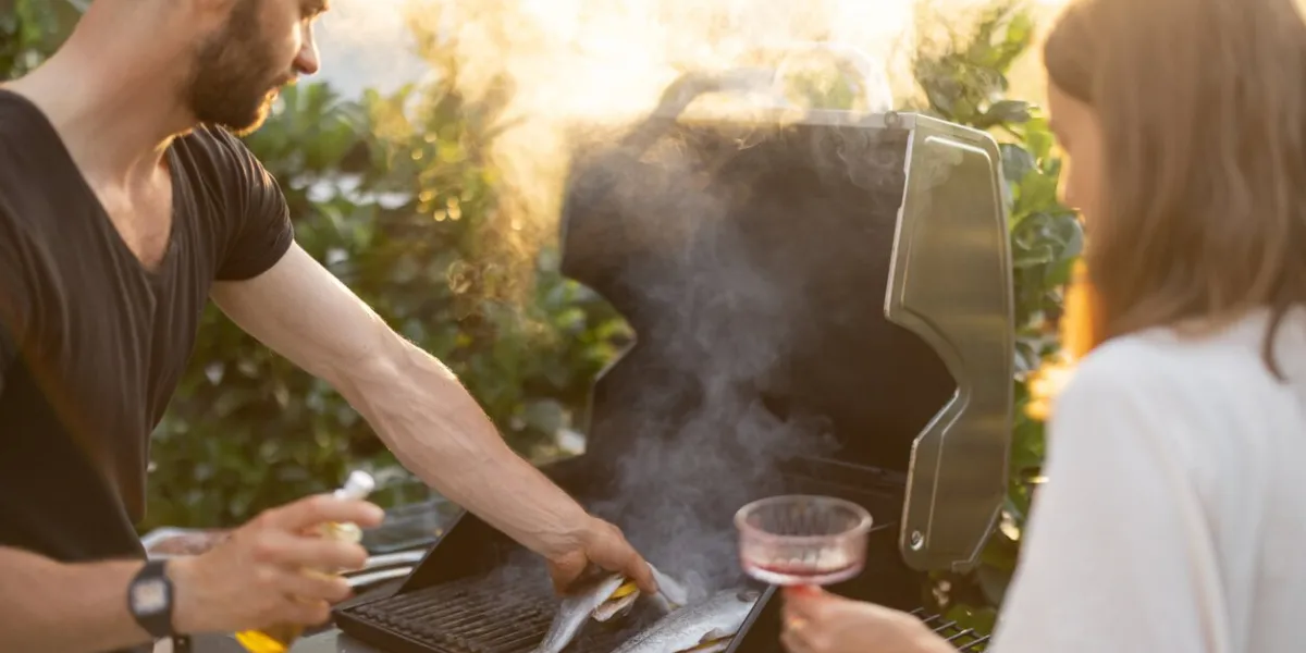 men cooking fresh trout fish on a modern gas grill outdoors at sunset cooking healthy food on the open air