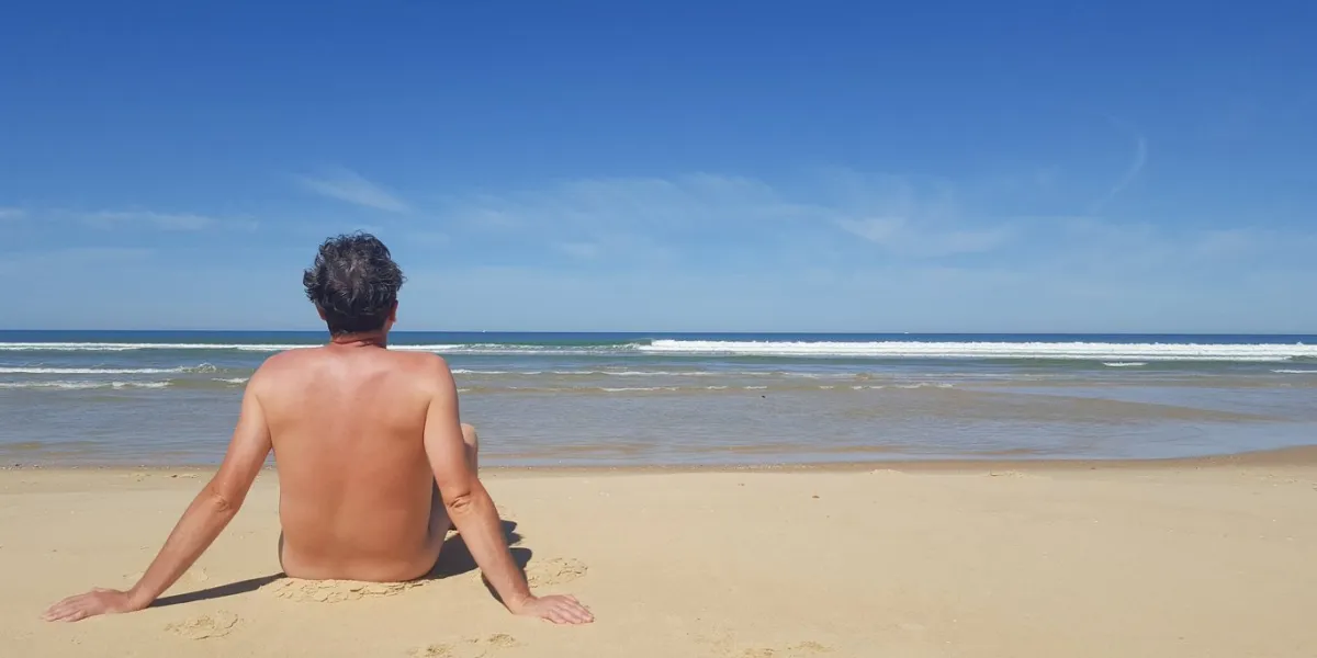 colour portrait photo of a naked man sitting alone on the beach