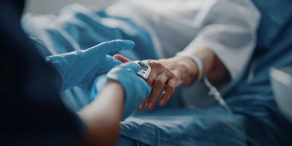 hospital ward  senior female resting in a bed nurse has finger heart rate monitor   pulse oximeter showing pulse anonymous nurse checks vitals of woman getting well after surgery