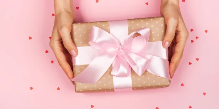 beautiful female hand with minimalistic gift on a pink background with cute hearts concept of the valentine's day, surprises with love, holiday, etc