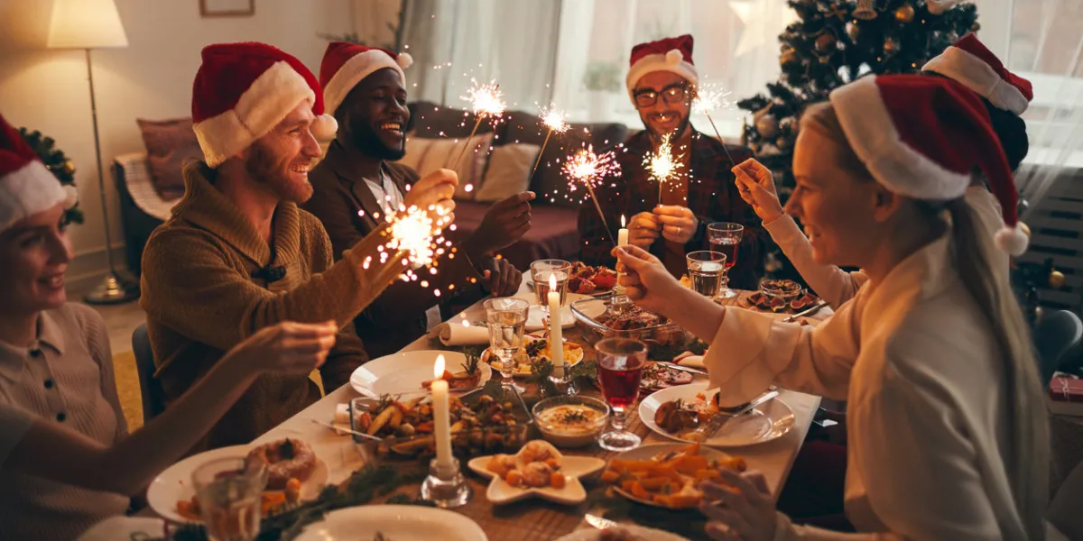 multi-ethnic group of people holding sparklers while enjoying christmas dinner at home