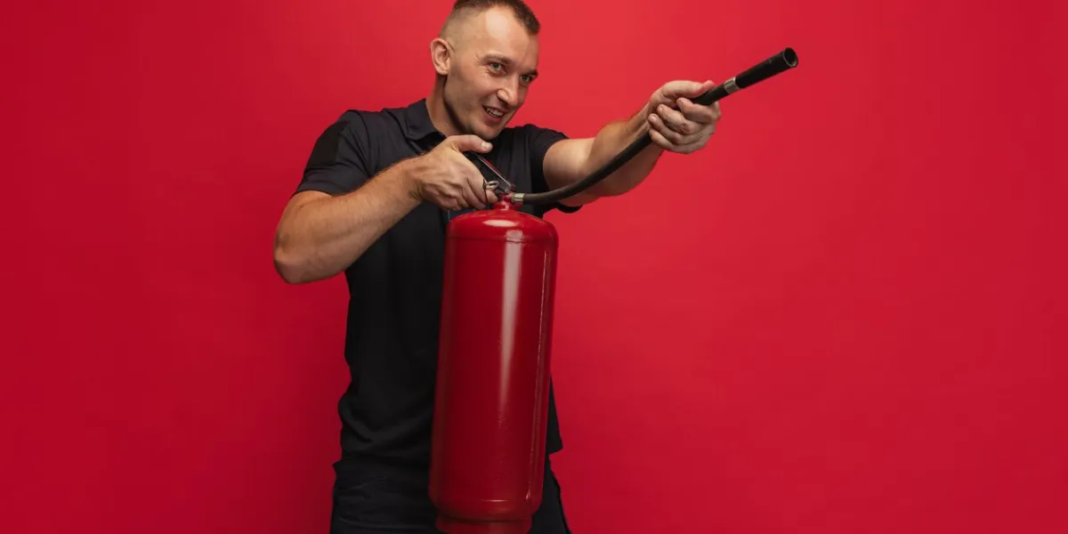 fireman one young smiling caucasian man posing with extinguisher in his hands posing over red background concept of different professions, unusual people and their emotions