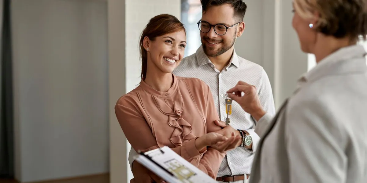 happy couple buying new home and receiving house keys form real estate agent