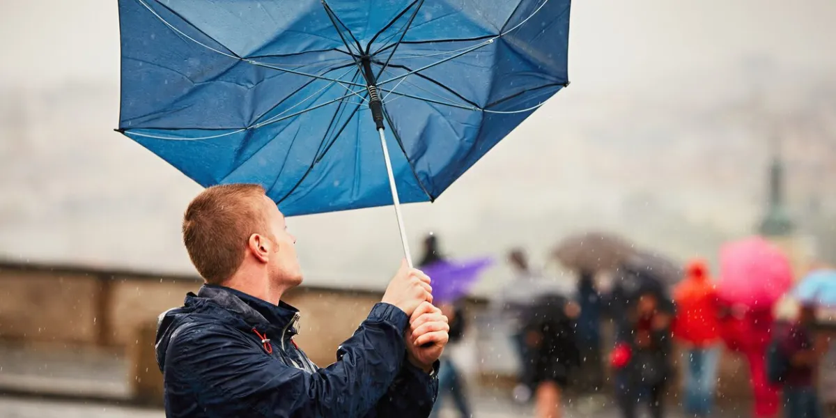 rain in the city young man is holding blue umbrella during thunderstorm street of prague, czech republic