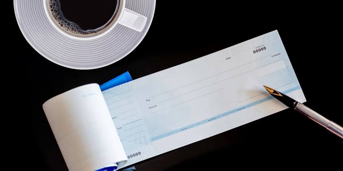 mockup image of checkbook, pen and white cup of coffee isolated on dark table background paycheque and payroll concept top view flat lay
