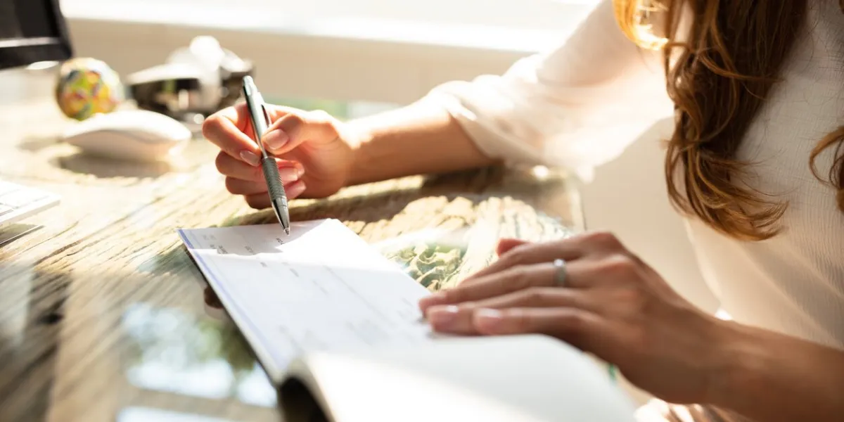 businesswoman's hand signing cheque on wooden desk