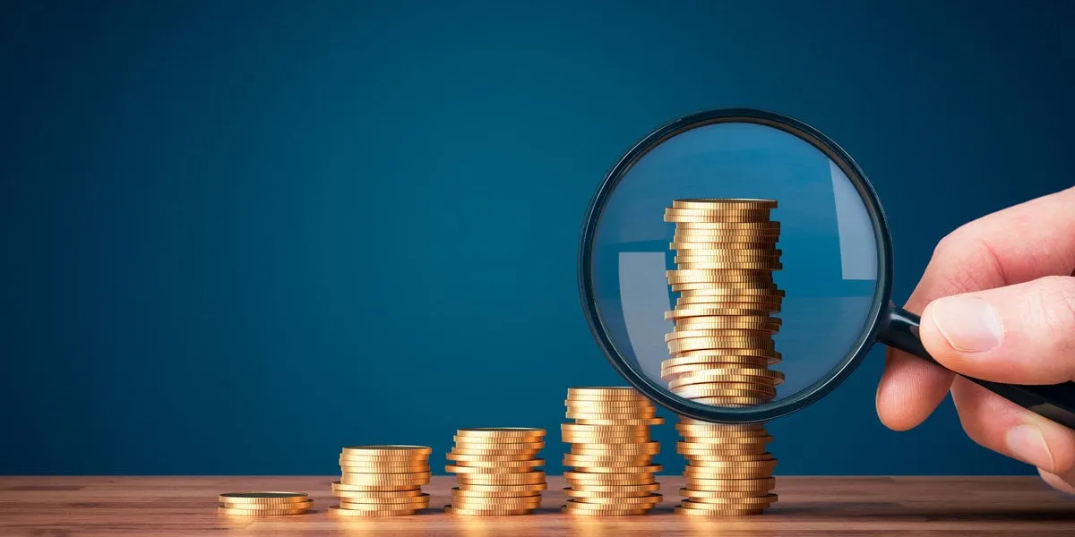 money makes money investment concept with magnifying glass coins in shape of growing graph and focus on the biggest column