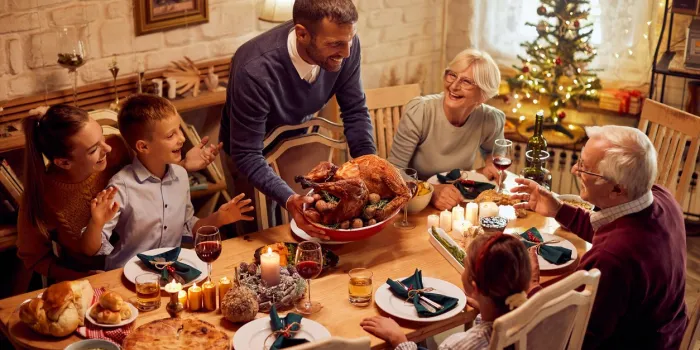 happy extended family celebrating thanksgiving and having traditional meal at dining table focus is on man serving roast turkey