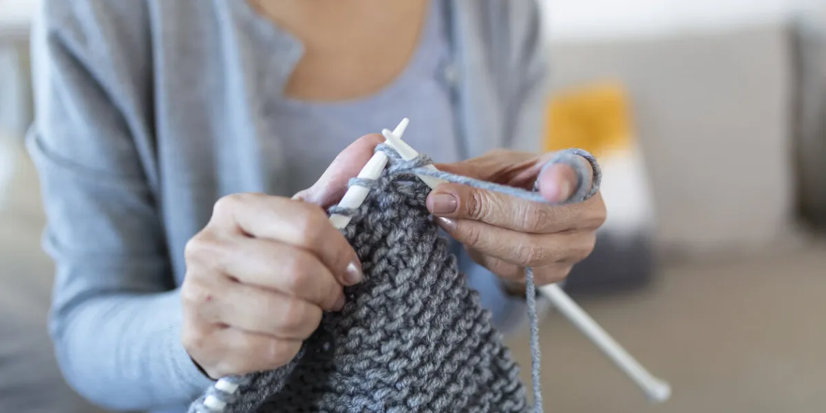 grandmother holding needles make repetitive motion knitting sitting on couch creating something with her arms hand knitting improve brain function, older generation hobby concept