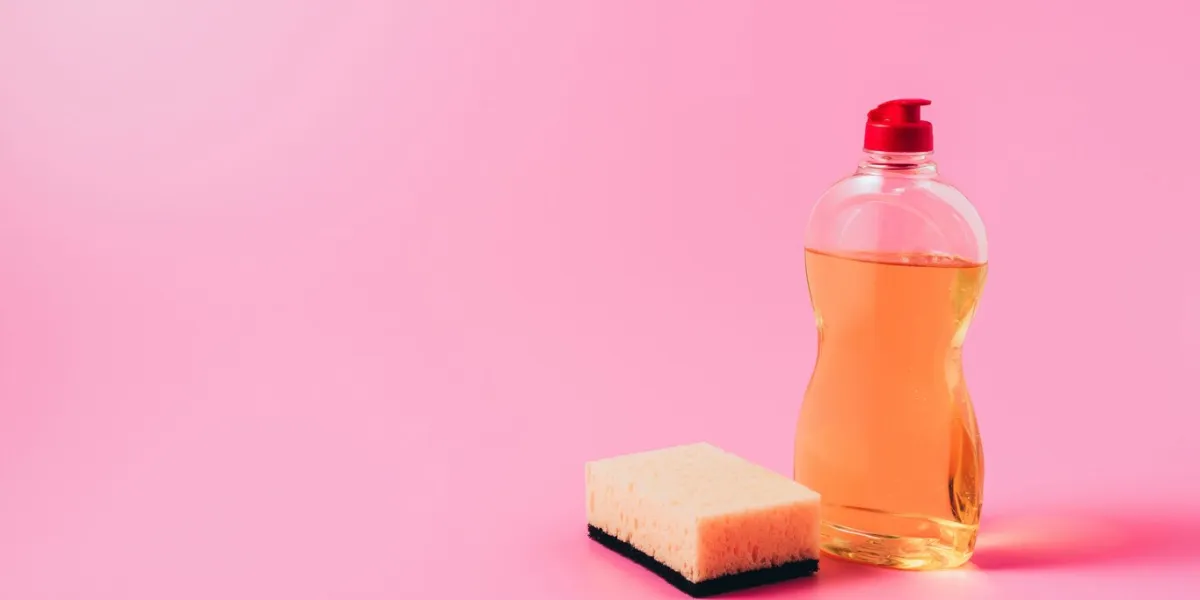 close up view of dishwashing liquid and washing sponge, pink background