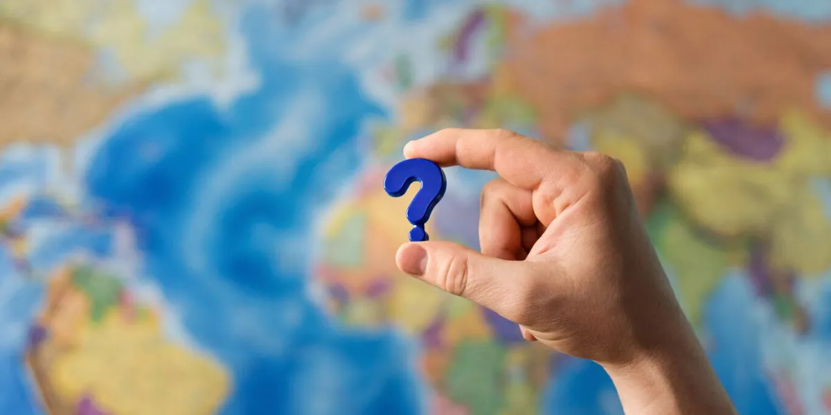adult hand holding question mark plastic toy on the world political map background travel planning explore destination concept quarantine over, borders open