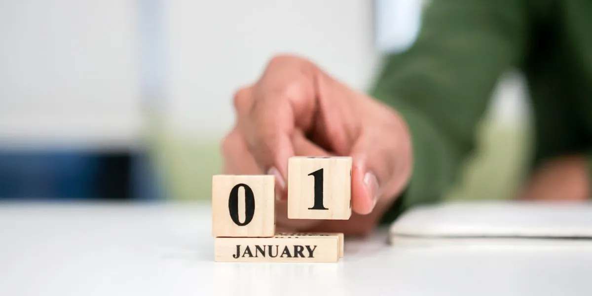 close up employee man hand put number 1 of cube shape wood to make calendar date january at office desk for the new day in first date of the year countdown concept