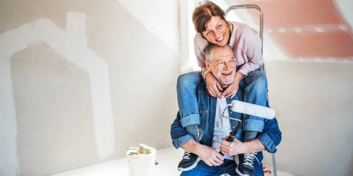 portrait of cheerful senior couple painting walls in new home, having fun relocation concept