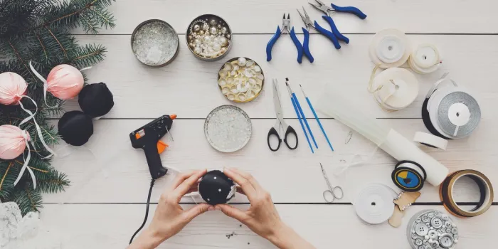 creative diy hobby making handmade craft christmas balls woman's leisure, tools for creating holiday decorations, pliers, glue gun and scissors top view of white wooden table with female hands
