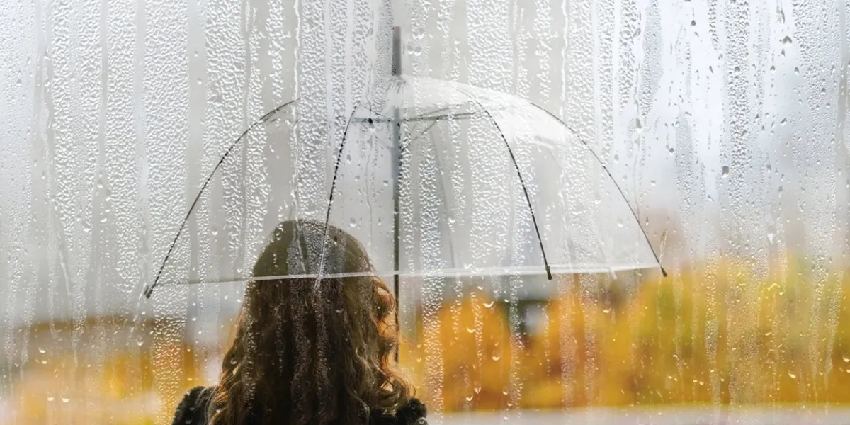 a woman silhouette with transparent umbrella through wet window with drops of rain autumn