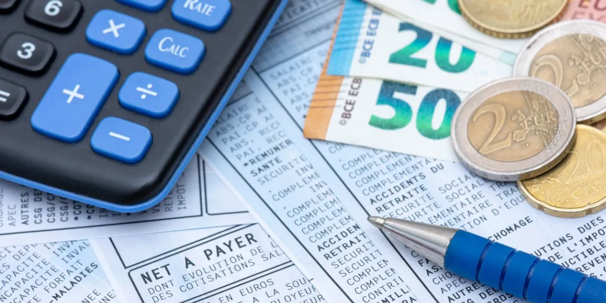 french payroll with social contributions and income tax deduction, mandatory in france since january 2019, along with a calculator, a pen, and euro coins and bank notes