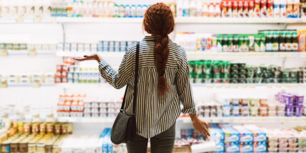 young woman in striped shirt from back trying choose dairy products in modern supermarket