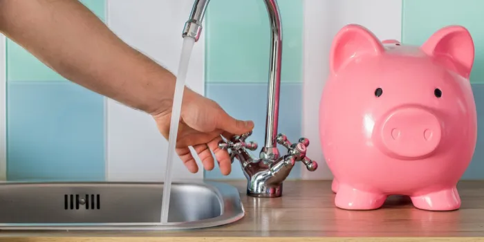 flowing tap water and a piggy bank standing next to it water consumption price concept