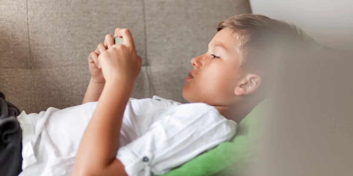 little boy using smart phone while relaxing on sofa in the living room