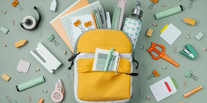 opened school backpack with stationery on green background concept back to school school supplies