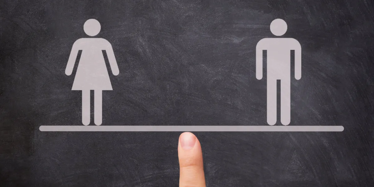 male equals female, women equal men, finger maintaining balance with a balance between man and woman on seesaw against a blackboard gender equality concept