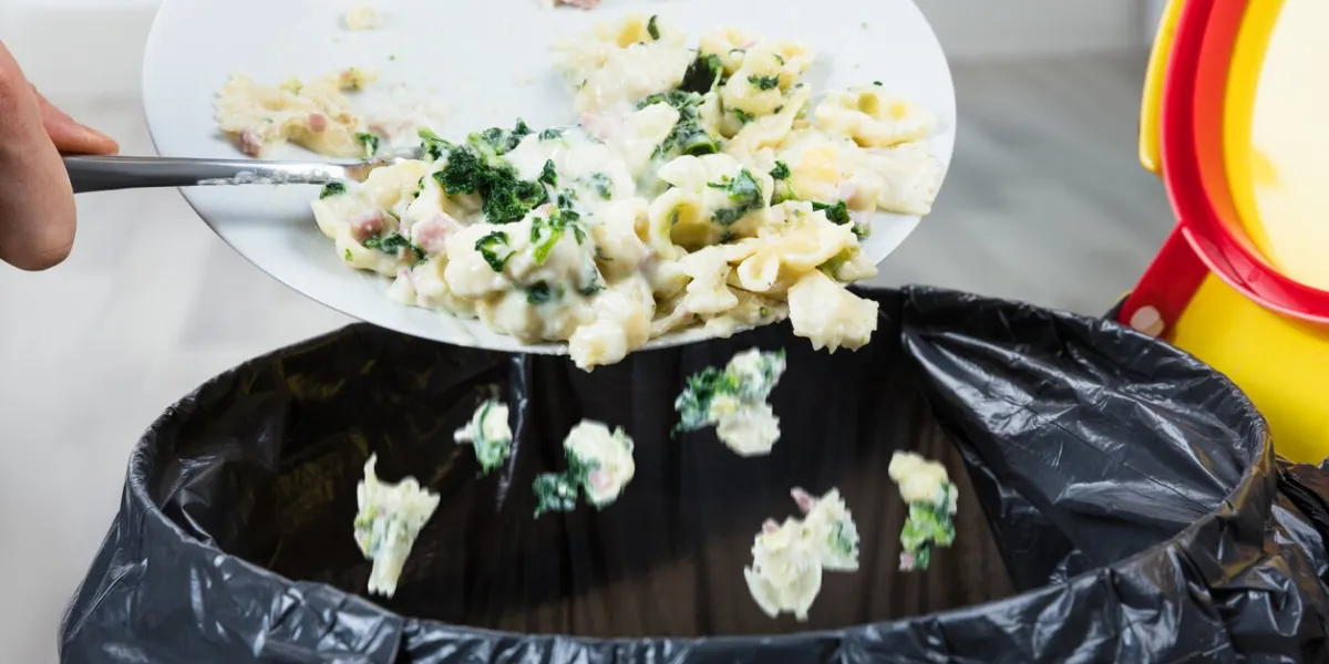 close-up of a person throwing the leftover pasta into the trash bin