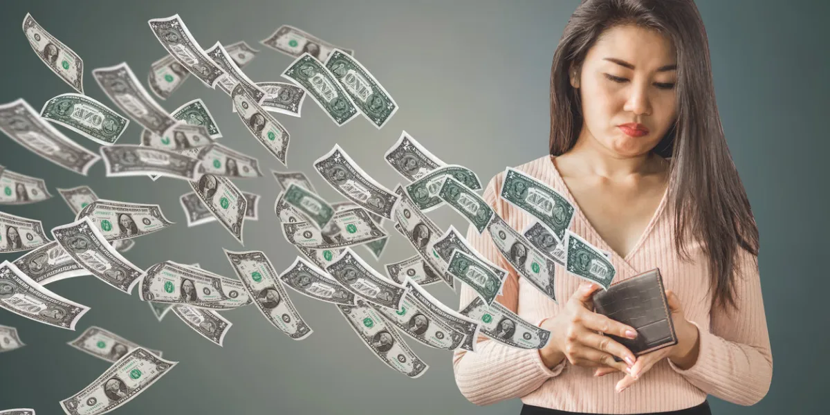 unhappy and poor asian woman holding purse having problem with money flying away, over spending concept background