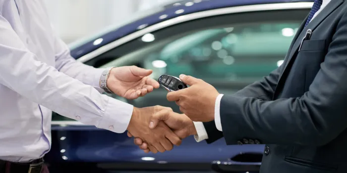 salesman giving car keys to customer and shaking his hand