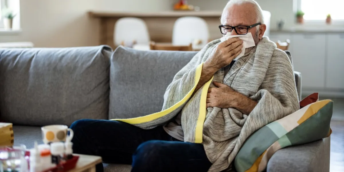 senior man at home suffering with cold or flu virus shot of a senior man blowing his nose with a tissue at home