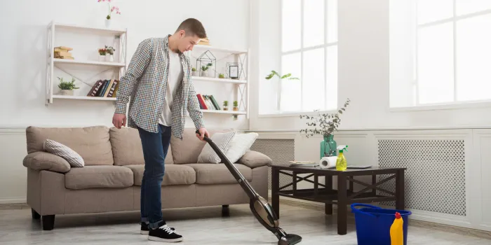 young man cleaning house, washing floor with vacuum cleaner, copy space