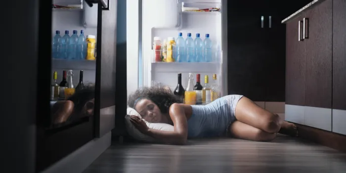 young hispanic woman suffering for summer heat and lack of air conditioning at home black girl covered with sweat sleeping on floor with head inside fridge