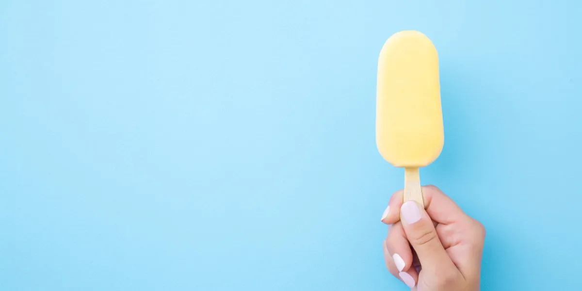 young woman hand holding ice cream with white chocolate glaze on pastel blue background top view closeup