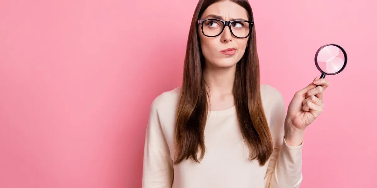 portrait of attractive suspicious girl using loupe copy space ad isolated over pink pastel color background