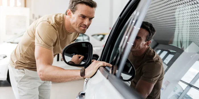 smiling man expressing concernment while looking at passenger compartment through window of automobile