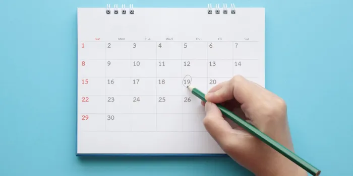 hand with pencil mark on calendar date on blue background