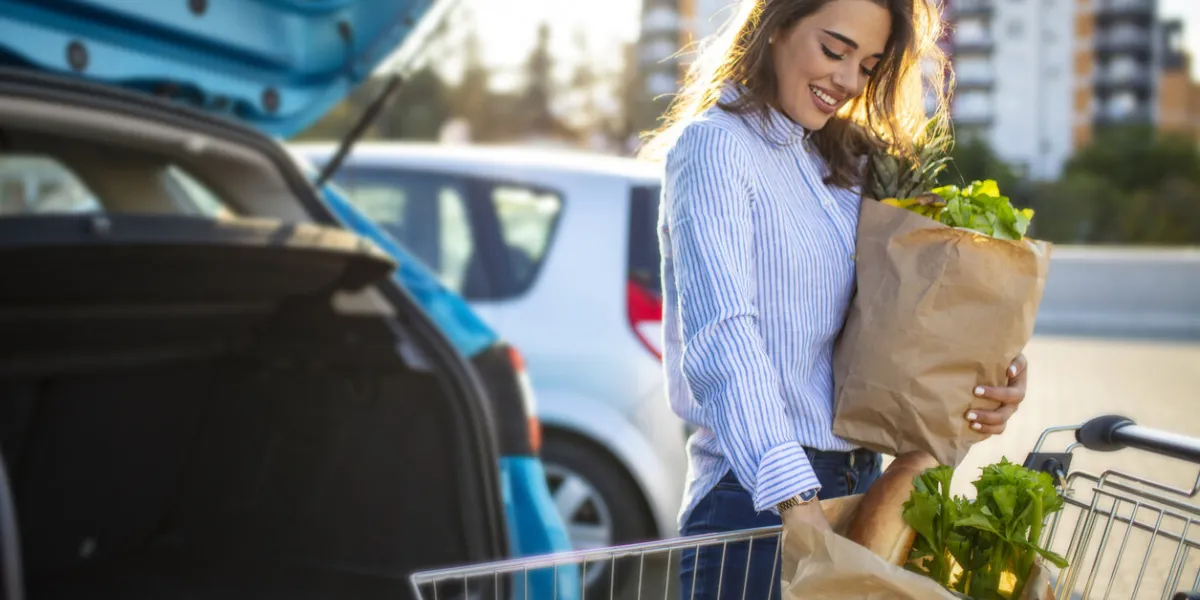 caucasian brunette going holding paper bags with food products young woman putting package with groceries and vegetables into car trunk attractive caucasian female shopping in mall or grocery store
